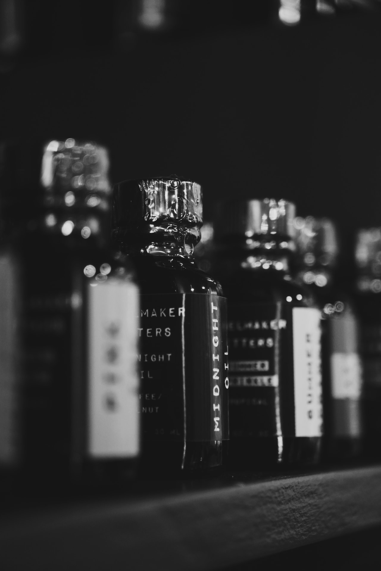Black-and-white close-up of spirit bottles lined up on a dark shelf
