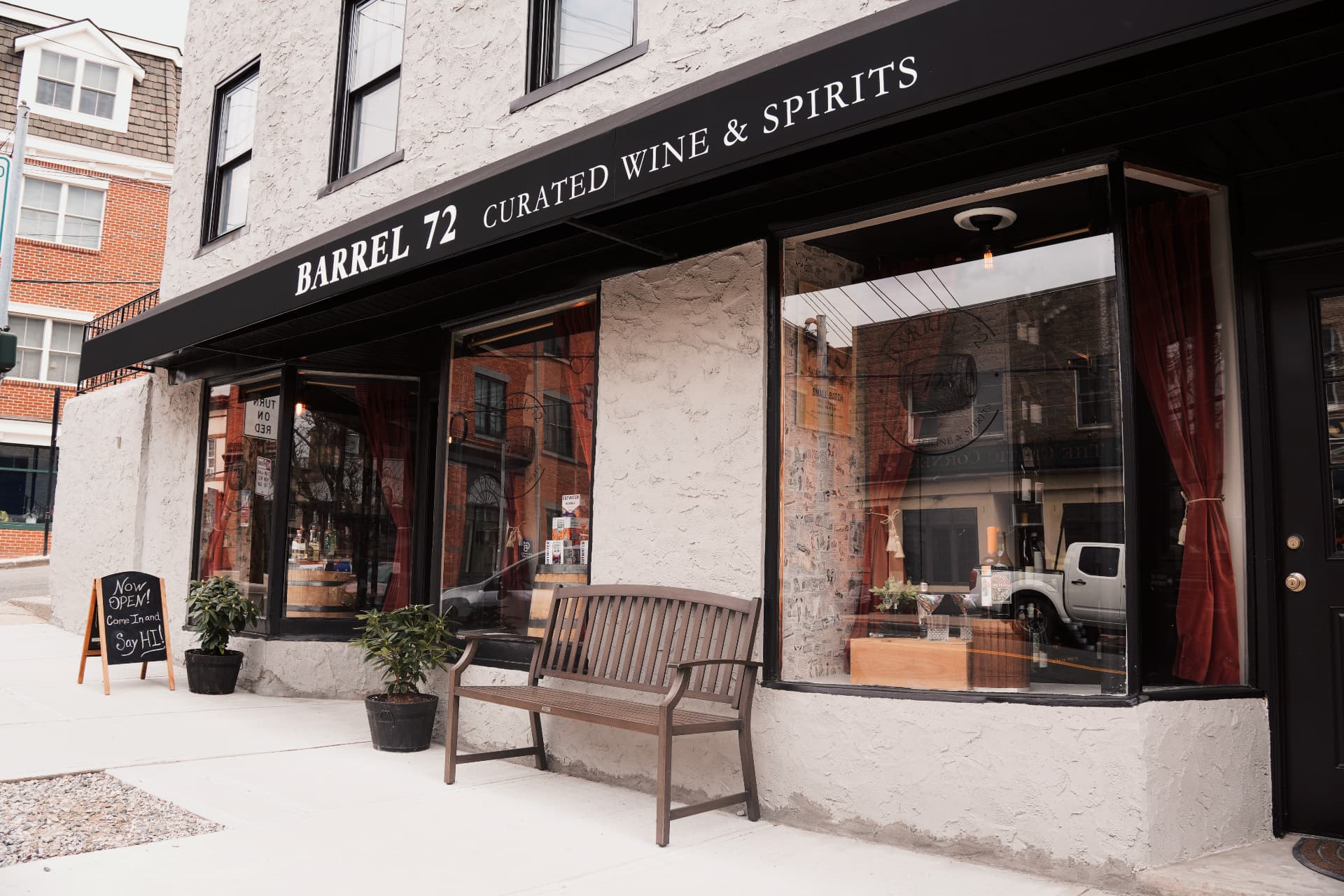The Barrel 72 Curated Wine & Spirits storefront in Dobbs Ferry, with a black awning and a wooden bench on the sidewalk