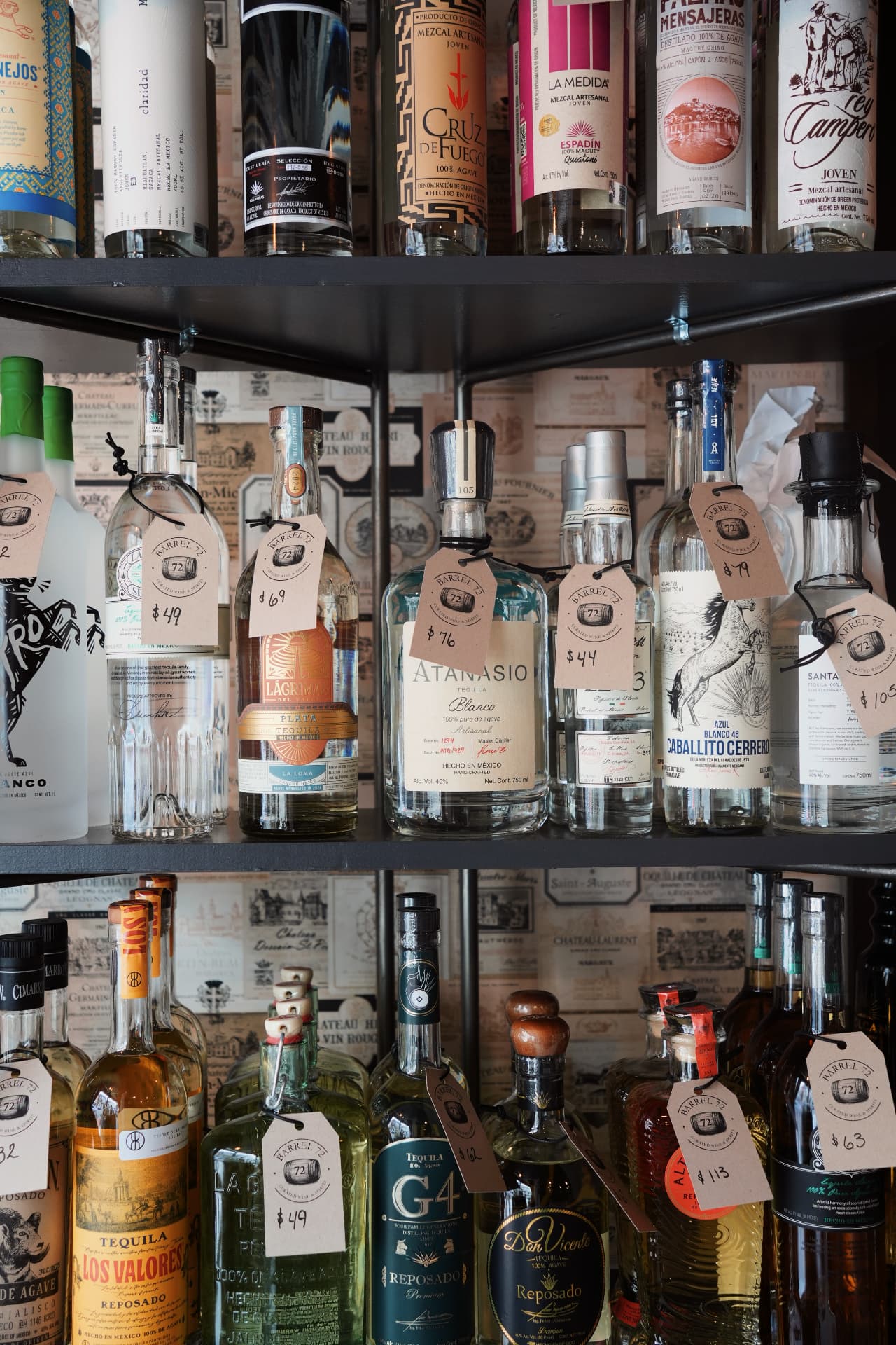 Three shelves of tequila and mezcal bottles, each with a handwritten Barrel 72 price tag