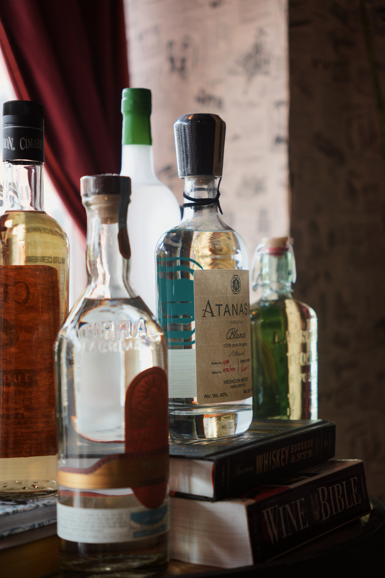 Blanco and reposado tequila bottles, including Atanasio, stacked on books by the Barrel 72 window