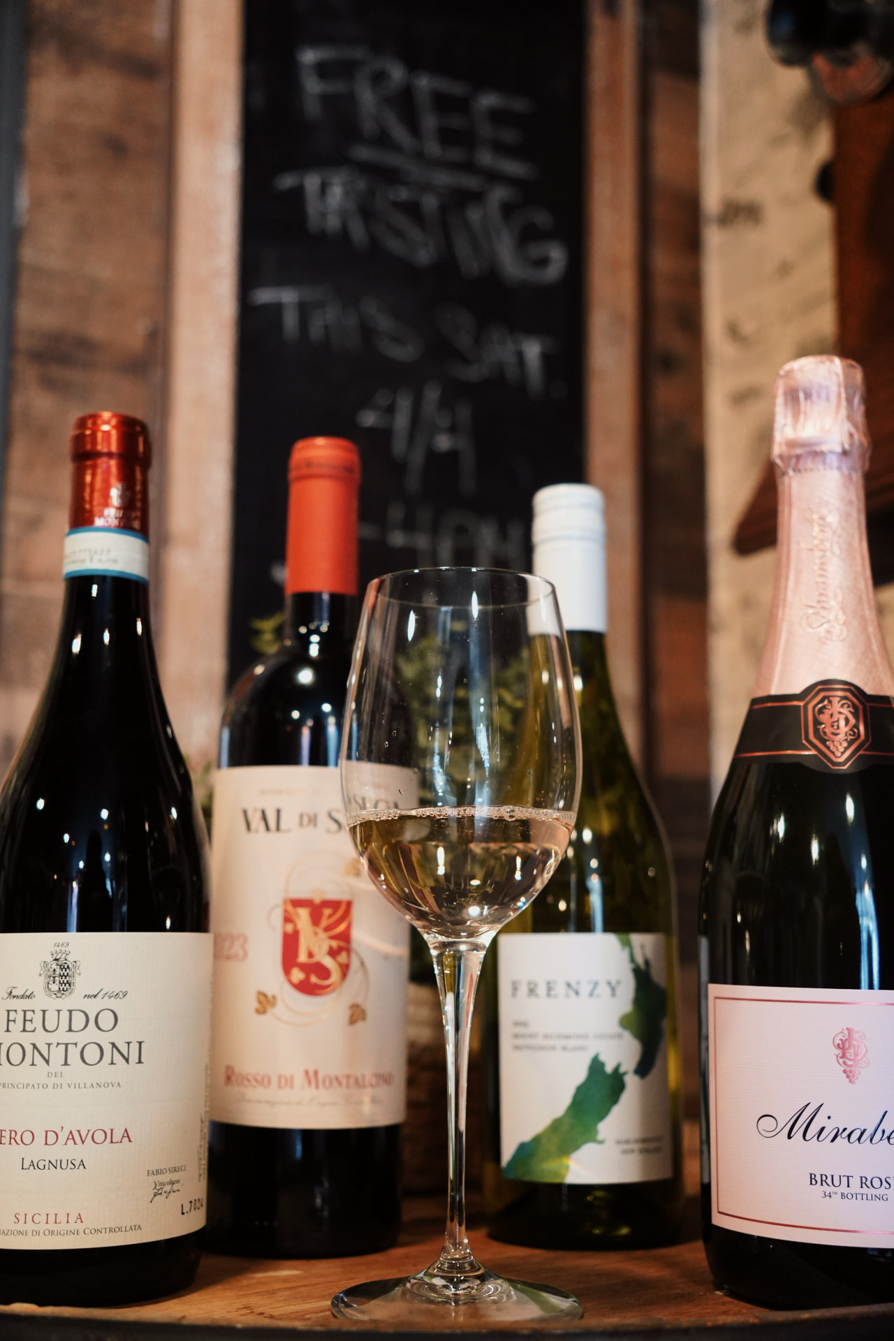 Four wines and a glass of white on the counter in front of a Free Tasting chalkboard at Barrel 72