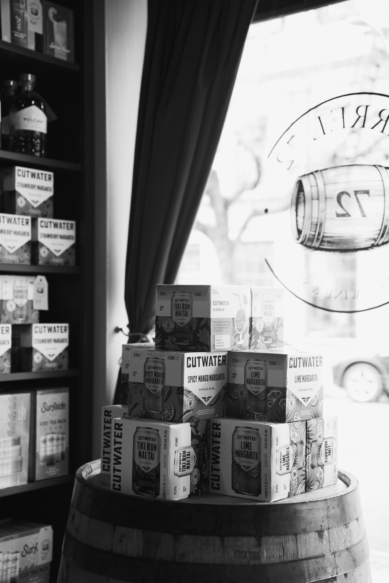 Black-and-white photo of Cutwater canned cocktail boxes stacked on a barrel by the Barrel 72 window