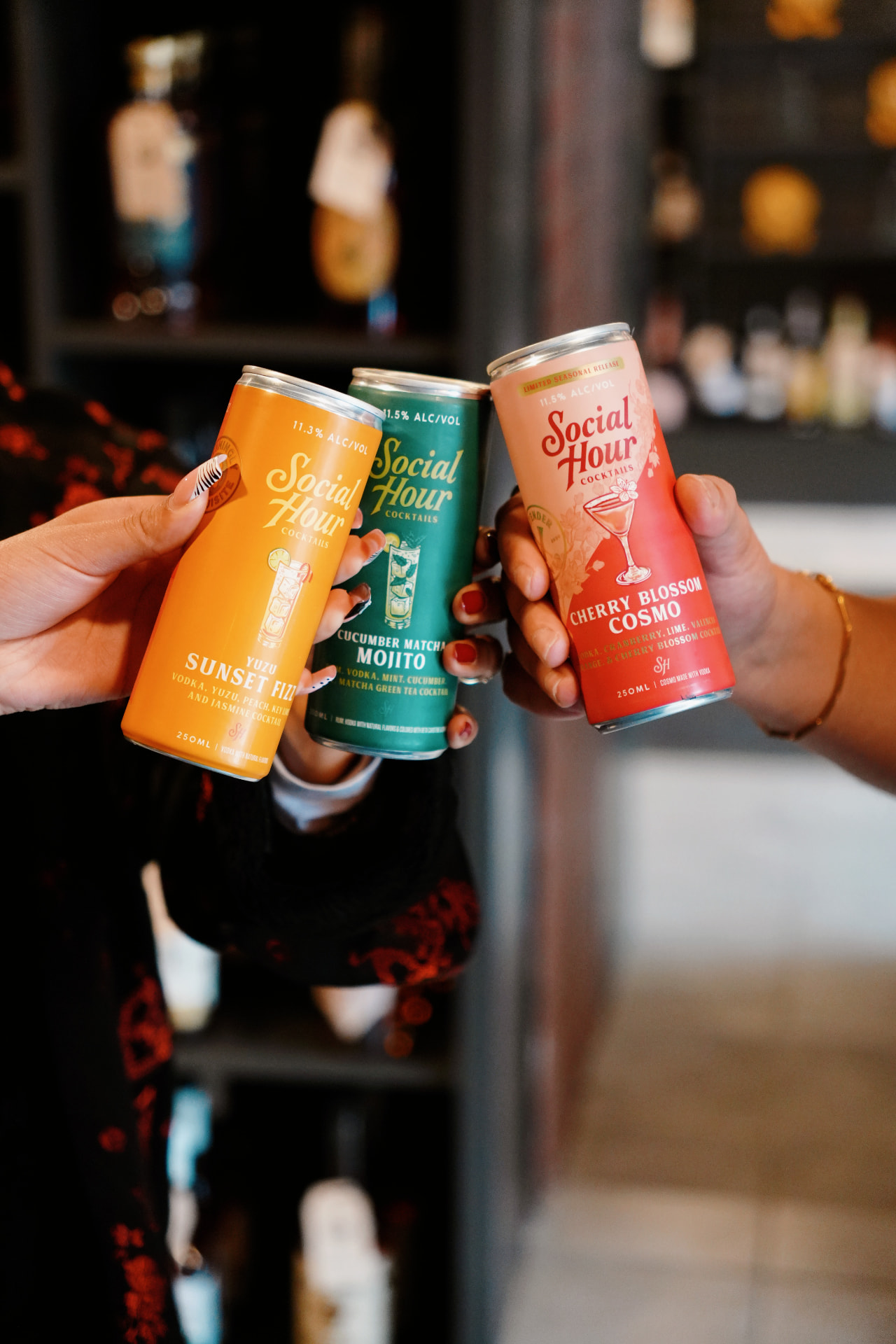 Hands toasting with three Social Hour canned cocktails inside Barrel 72